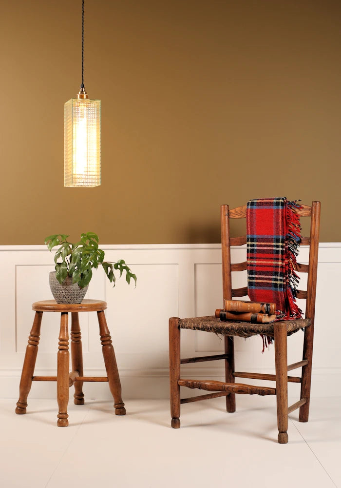 Wooden chair with a plaid blanket, wooden stool with plant, and pendant light in a room.