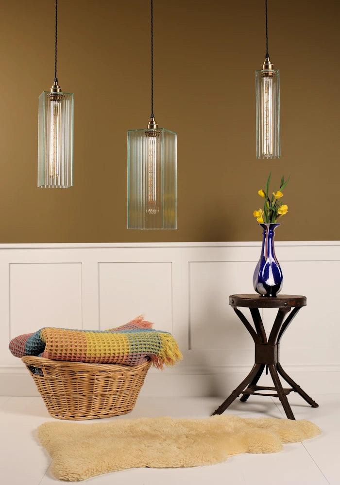 Living room with wicker chair, rug, and fluted glass art deco style pendant lights against a brown wall.