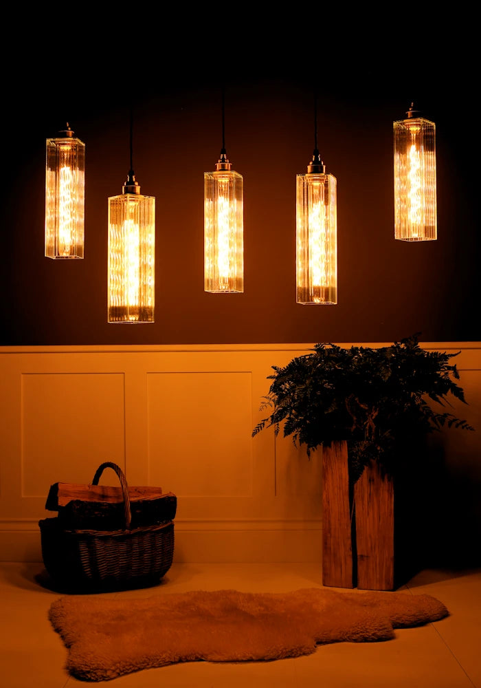 Decorative pendant lights hanging against a dark wall with a plant and basket on a light-colored floor.