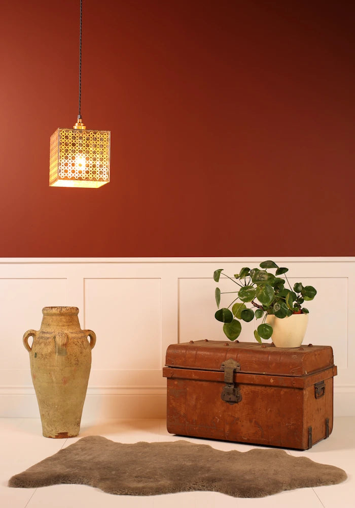 Cube gold leaf pendant light with Moroccan style pattern hanging over vase, vintage trunk, plant on red background