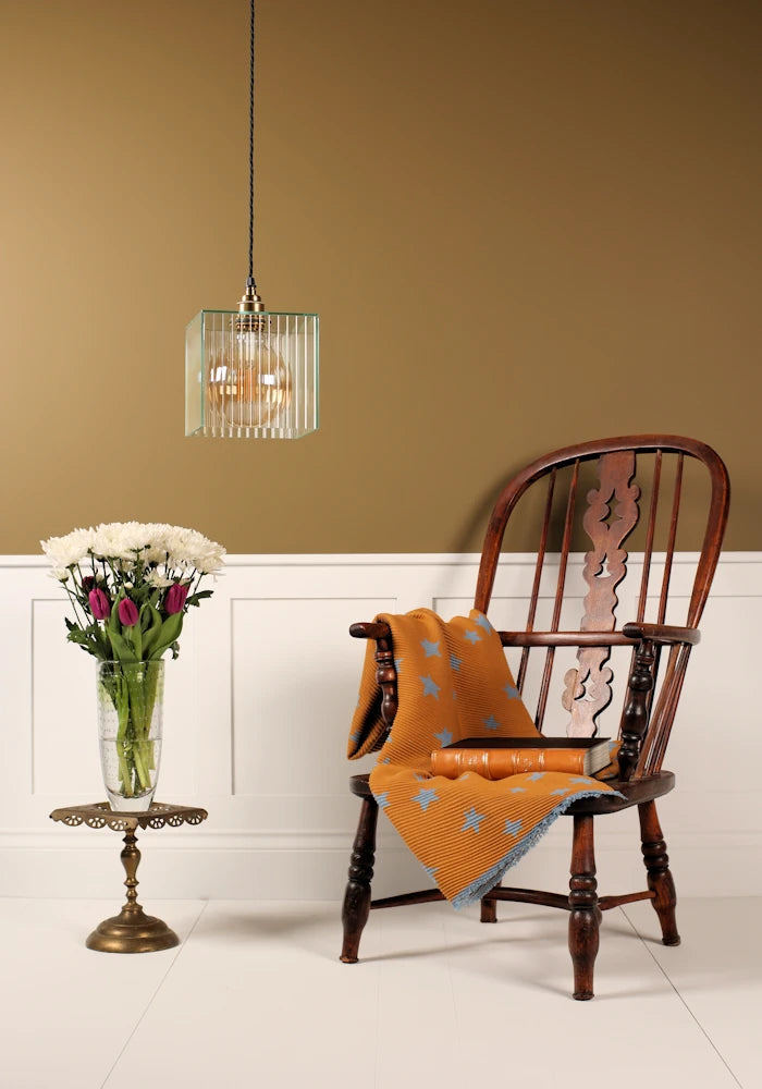 Wooden chair with an orange blanket, a small table with flowers, and a pendant light in a room.