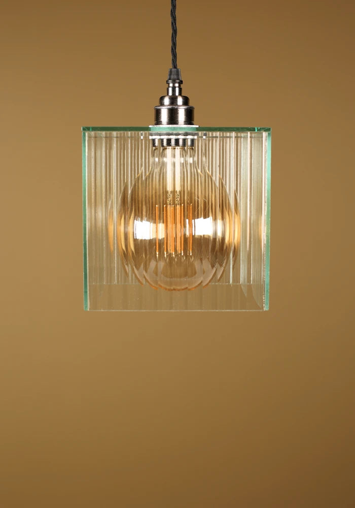Glass pendant light with nickel fixture on a beige background