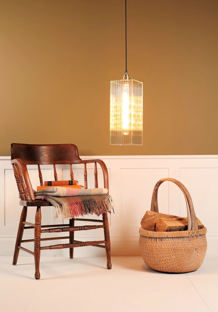 Wooden chair with a woven basket and a pendant light in a room with a yellow wall.