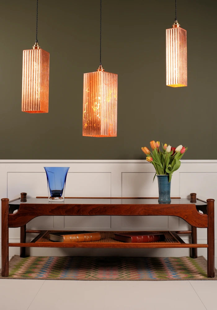Three copper pendant lights hanging above a wooden console table with decorative items.