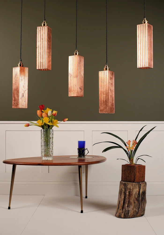 5 copper pendant light cluster hanging over coffee table with vase of tulips with green and white background.