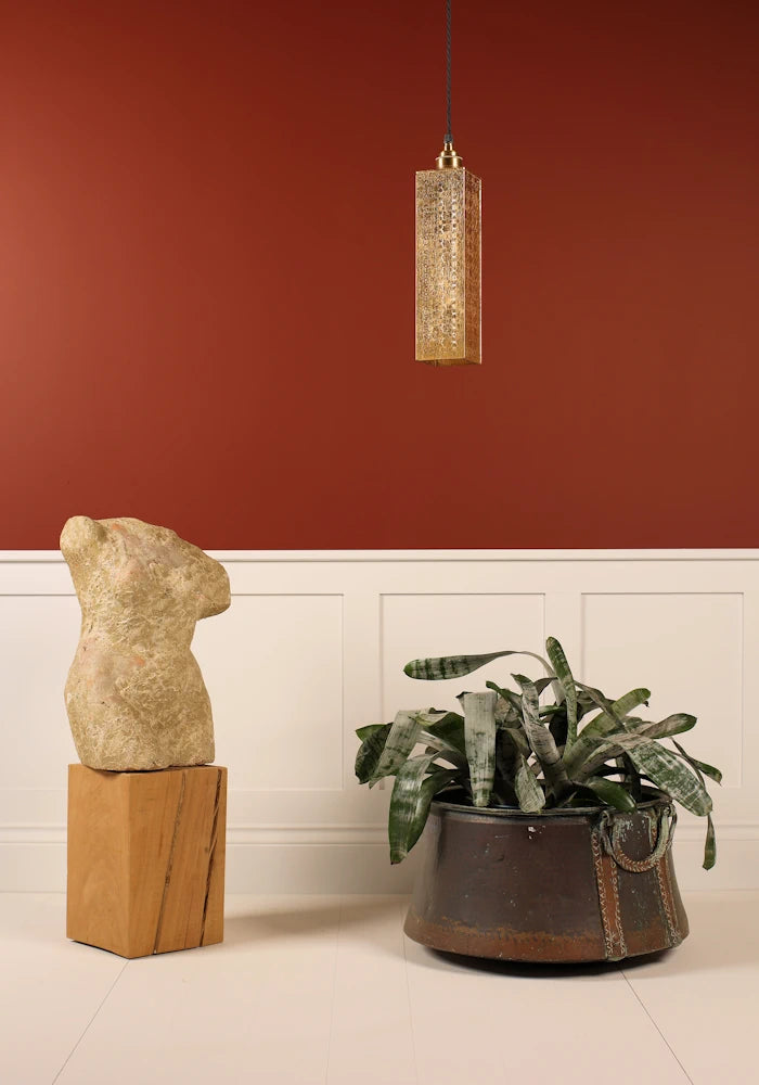 Elegant, rectangular Moroccan style gold pendant light hanging over plant with faux Italian marble bust statue and red background