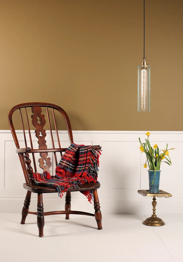 Wooden chair with a red plaid blanket, small table with flowers, and pendant light in a room.