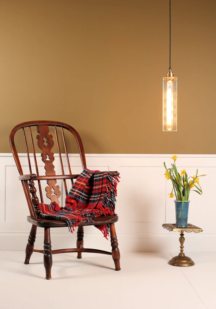 Wooden chair with a plaid blanket, small table with flowers, and pendant light in a room.