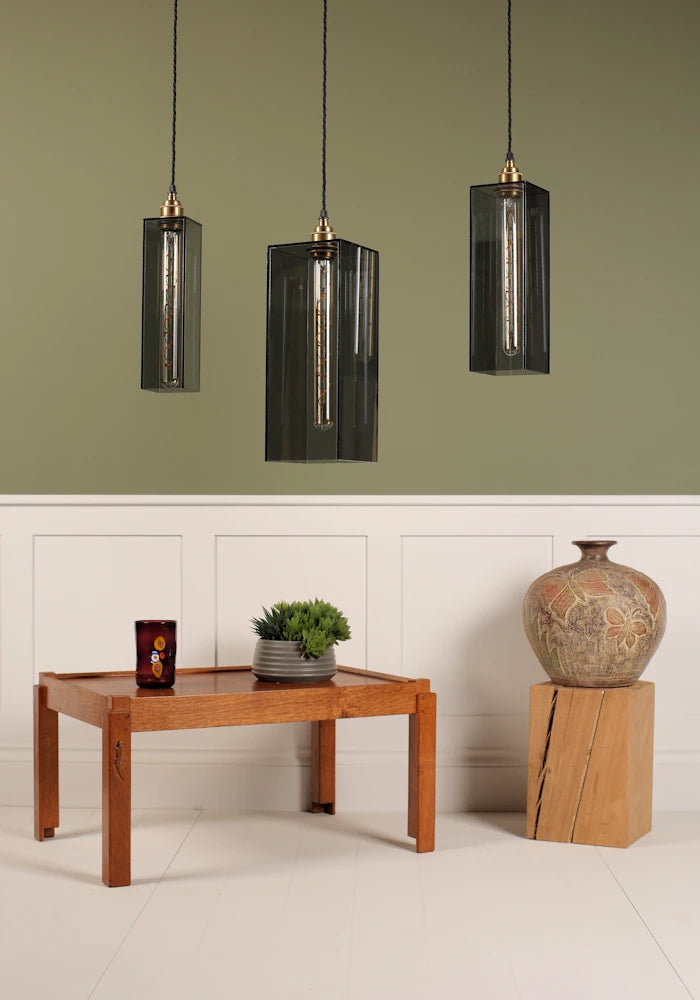 Three smoked glass pendant lights hanging above a wooden table with decor items on a light green wall.