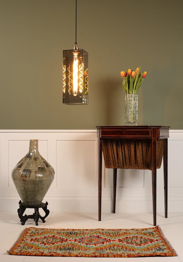 Large smoked glass pendant light, vintage dresser table with tulips, ornate floor vase on sage green background