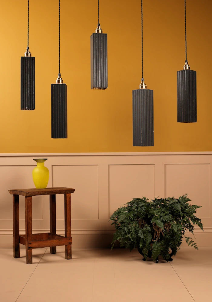 Black pendant lights hanging against a mustard yellow wall with a wooden side table and plant in the foreground.