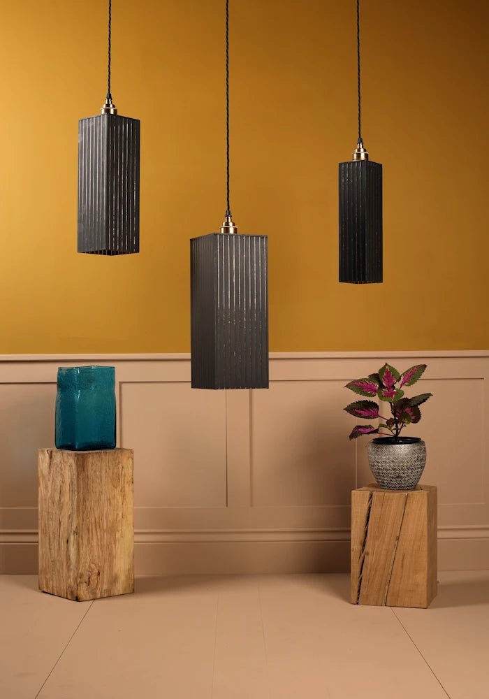Three black pendant lamps hanging against a mustard yellow wall with wooden stands and decorative items.