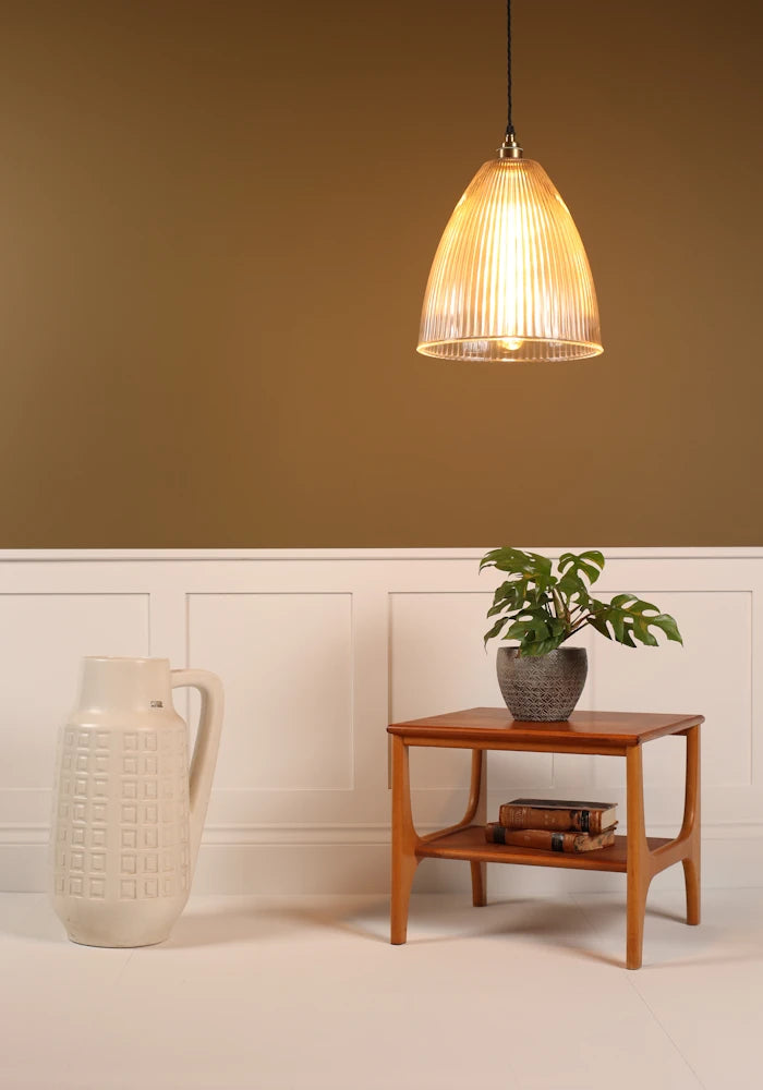 Large statement ribbed glass pendant light hanging over coffee table with plant, tall vase on beige background