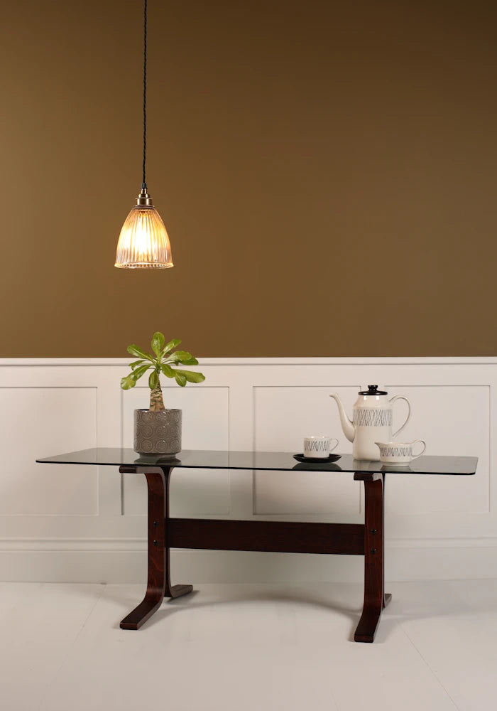 Small bell prismatic pendant light hanging over modern coffee table, plant, coffee pot on beige background
