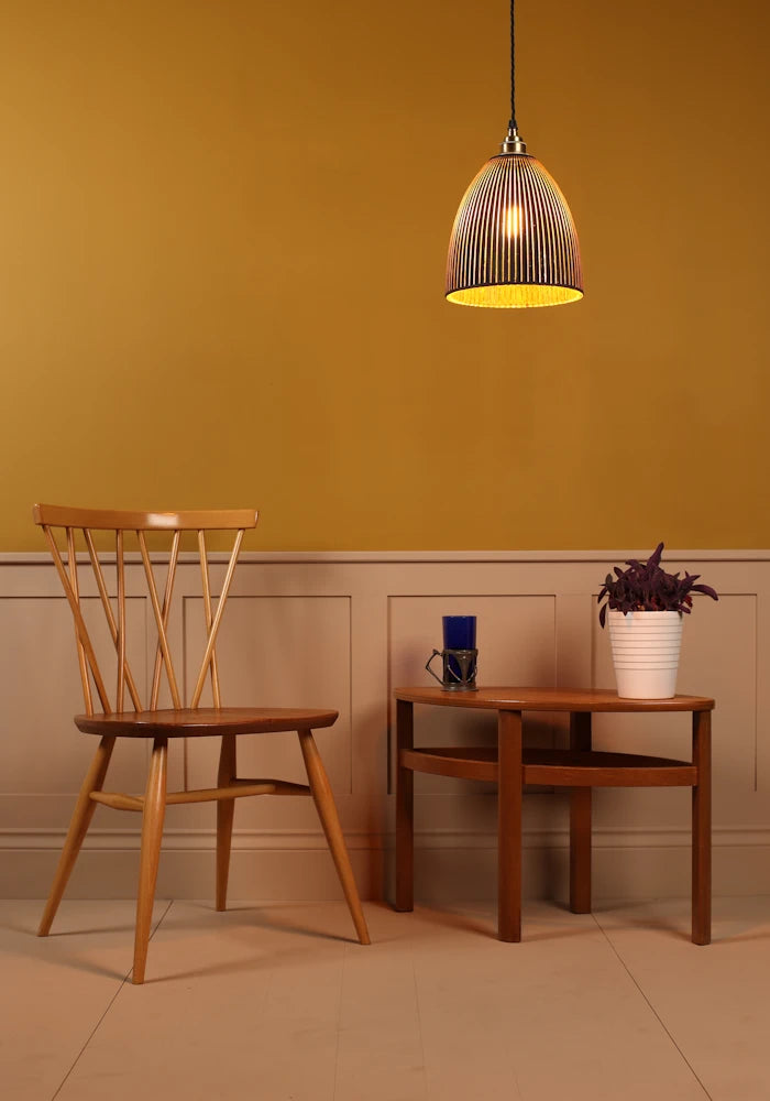 Black and gold pendant light hanging over wooden table with plant, designer wooden chair and yellow background