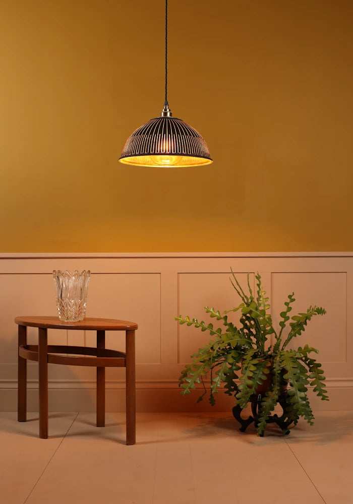 Black & gold dome prismatic glass pendant light hanging over coffee table, green leaf plant, on mustard yellow background