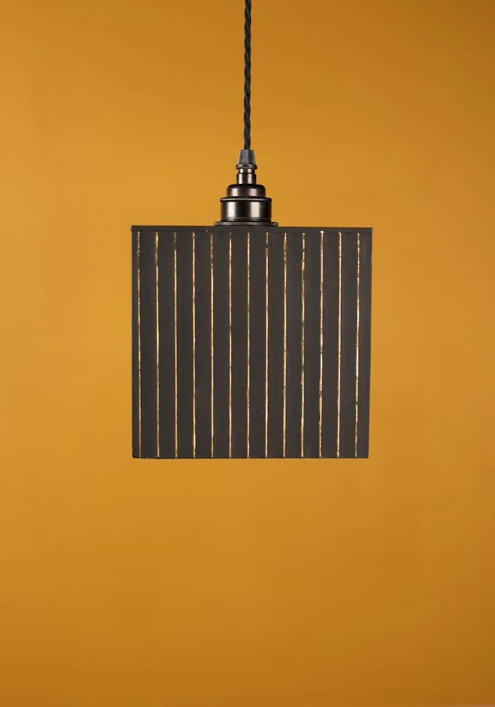 Black pendant light against a mustard yellow background with bronze lamp holder