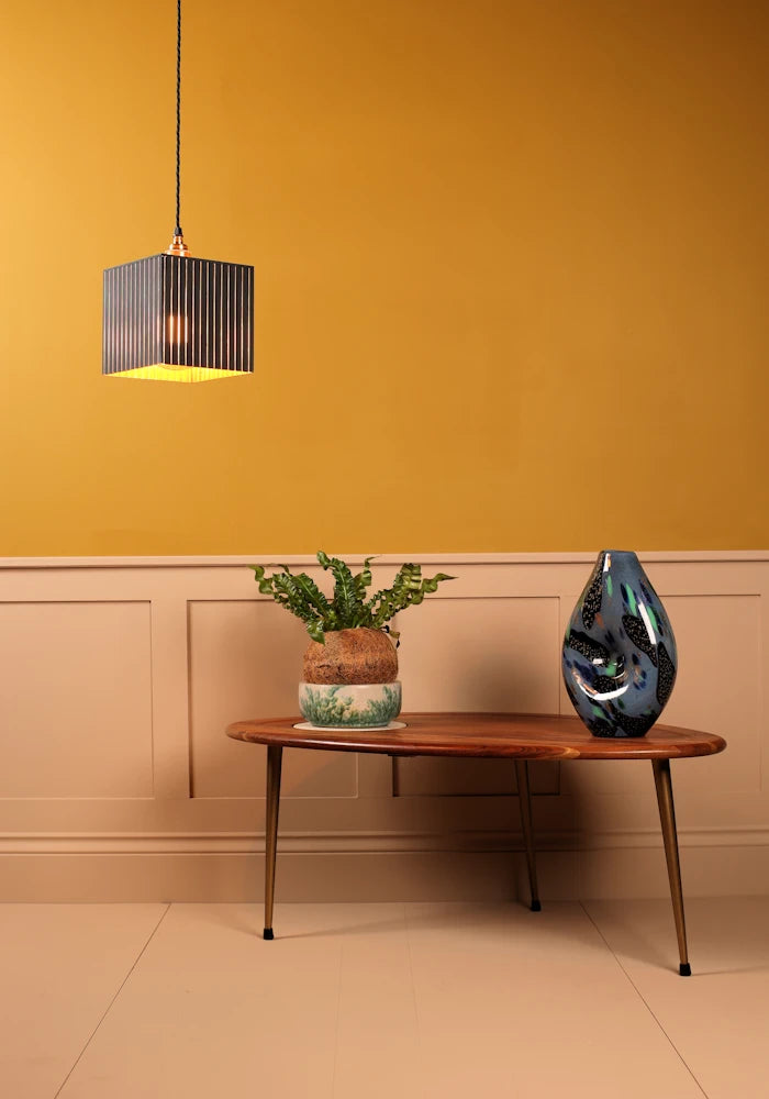 Modern interior with a wooden table, decorative plant, and vase against a mustard yellow wall.
