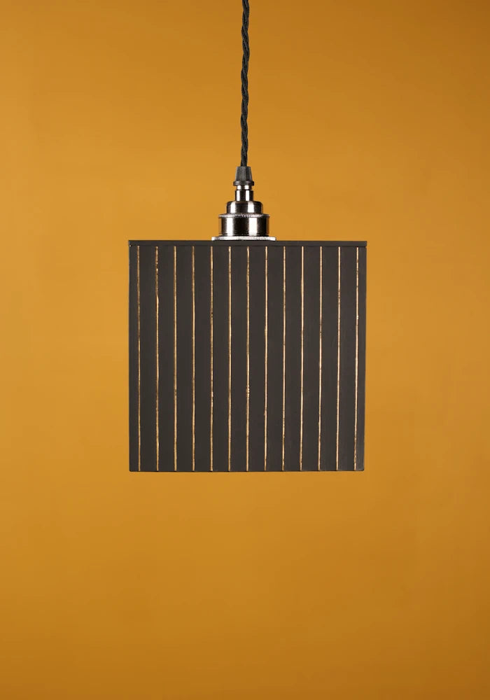 Pendant light with rectangular black shade on a mustard yellow background with nickel lamp holder