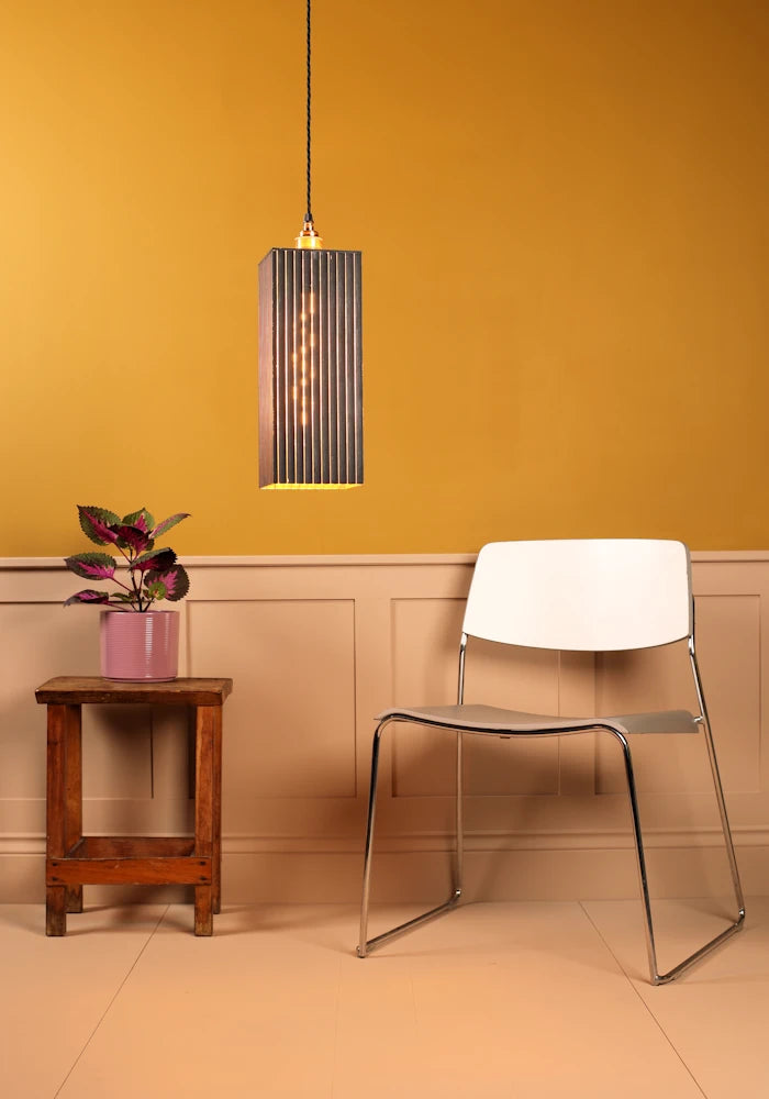 Modern chair against a mustard yellow wall with a pendant light and small table.