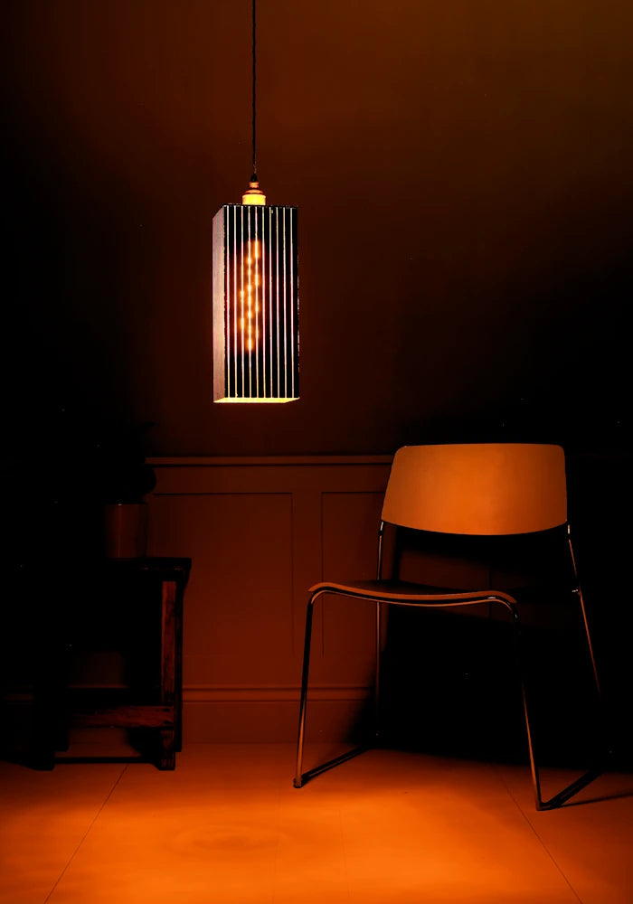 Large black & gold pendant light glowing in dark room with modern chair, plant and mustard coloured background