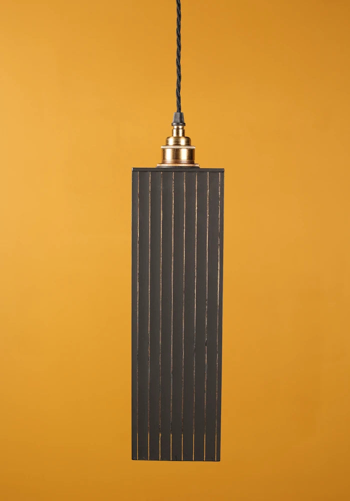 Pendant light with ribbed design against a mustard yellow background with brass lamp holder