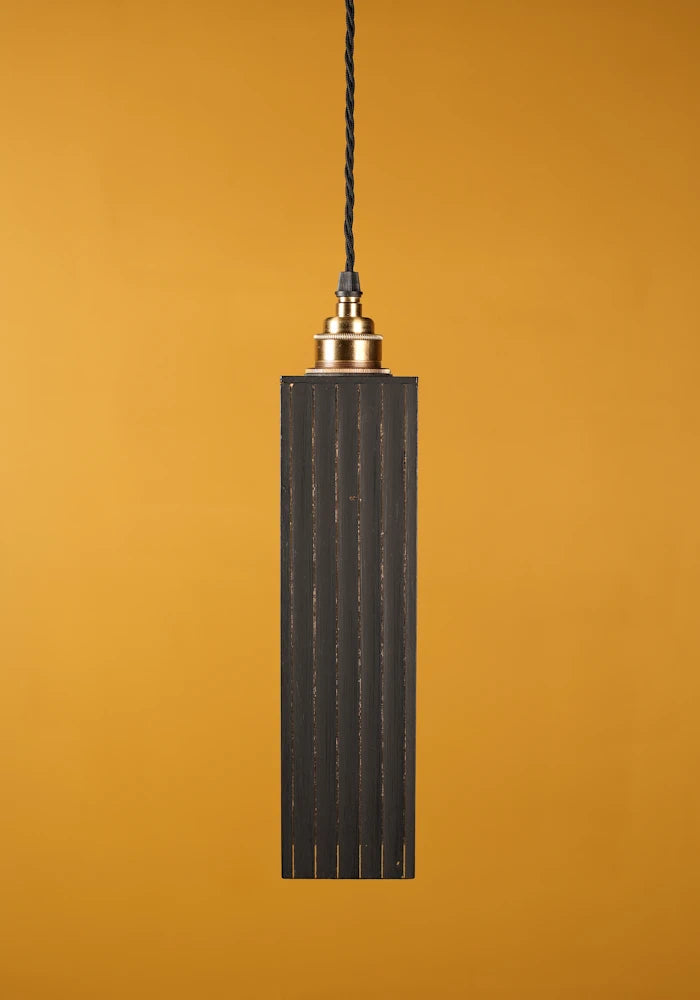 Black pendant light with gold fixture on a mustard yellow background with brass lamp holder