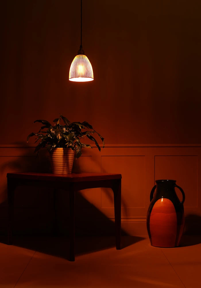 Black fluted glass pendant light, wooden table with a plant and a decorative vase in dimly lit room