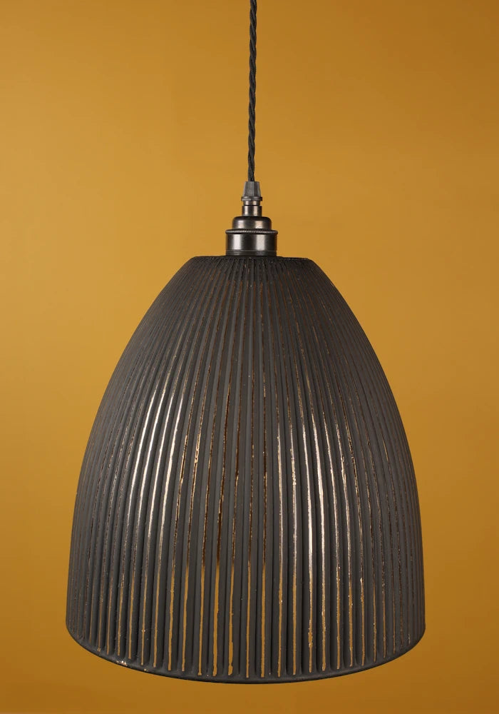 Black ribbed pendant light with bronze lamp holder against a mustard yellow background