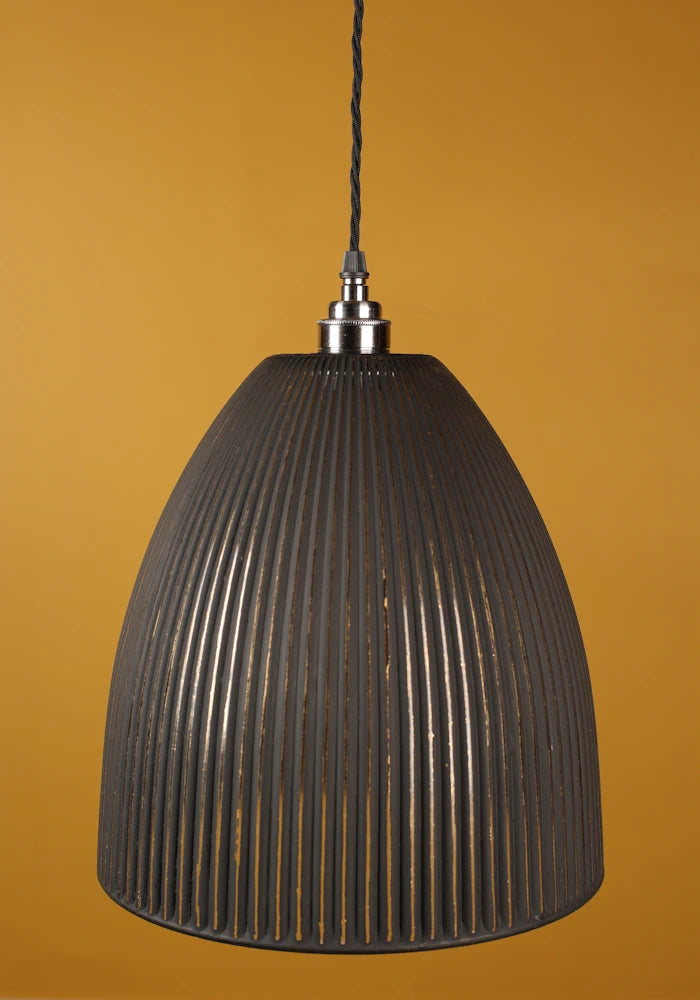Black ribbed pendant light with nickel lamp holder against a mustard yellow background