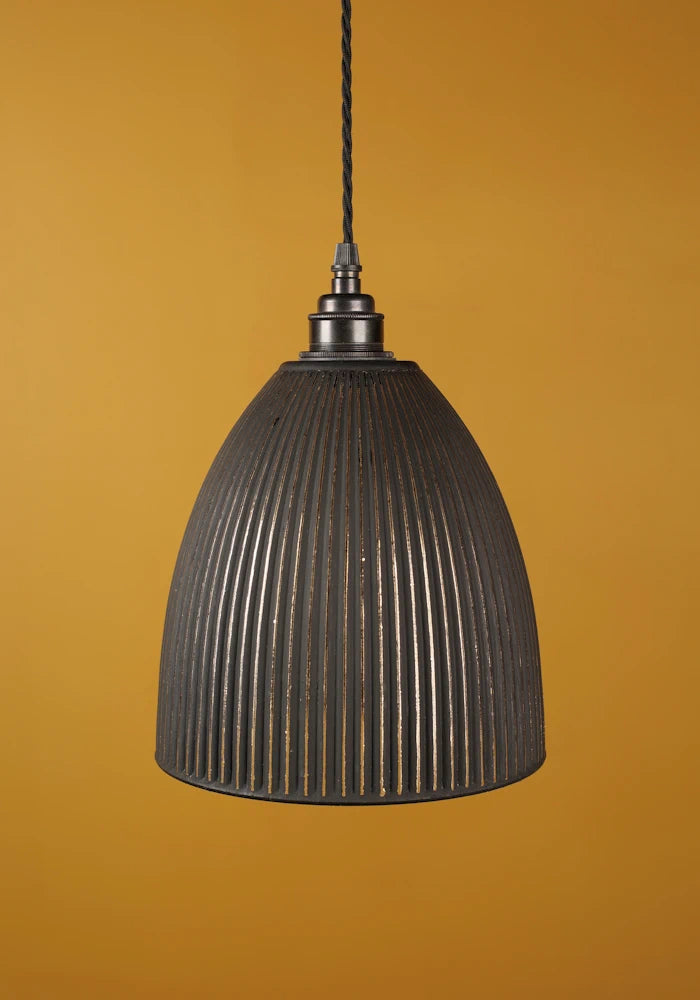 Black ribbed pendant light with bronze lamp holder against a mustard yellow background