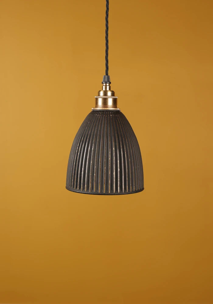 Black pendant light with brass lamp holder against a mustard yellow background
