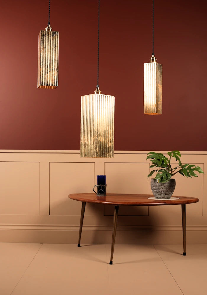 Three pendant lights hanging above a wooden table with a plant and small object in a room with a red wall and beige wainscoting.