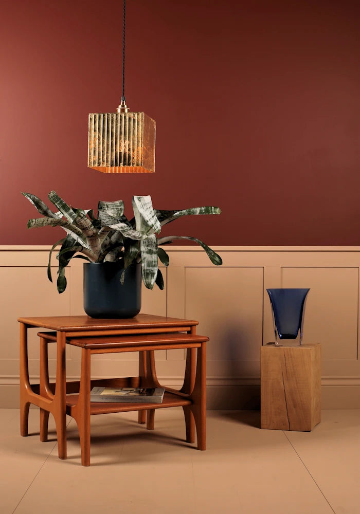 Gold leaf pendant cubed light hanging over plant with red and cream background