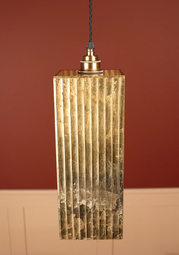 Decorative gold leaf pendant light with brass lamp holder against a red wall.