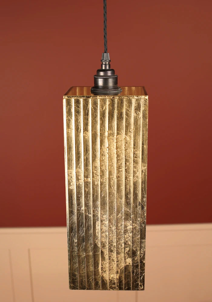 Decorative gold leaf pendant light with bronze lamp holder against a red wall.
