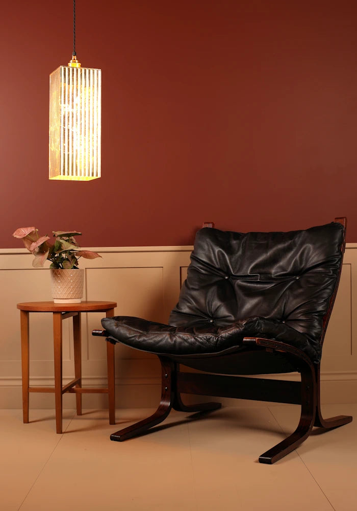 Large feature gold leaf pendant light, black leather chair in a room with a red wall and wooden side table.
