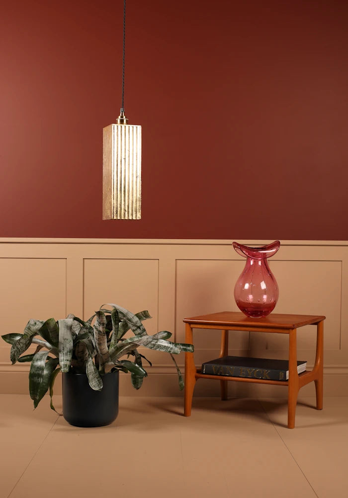 Modern interior with gold pendant light, plant, and table against a red wall.
