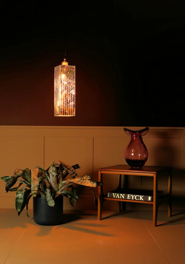 Decorative gold lamp hanging on a dark wall with a plant and a vase on a table below.