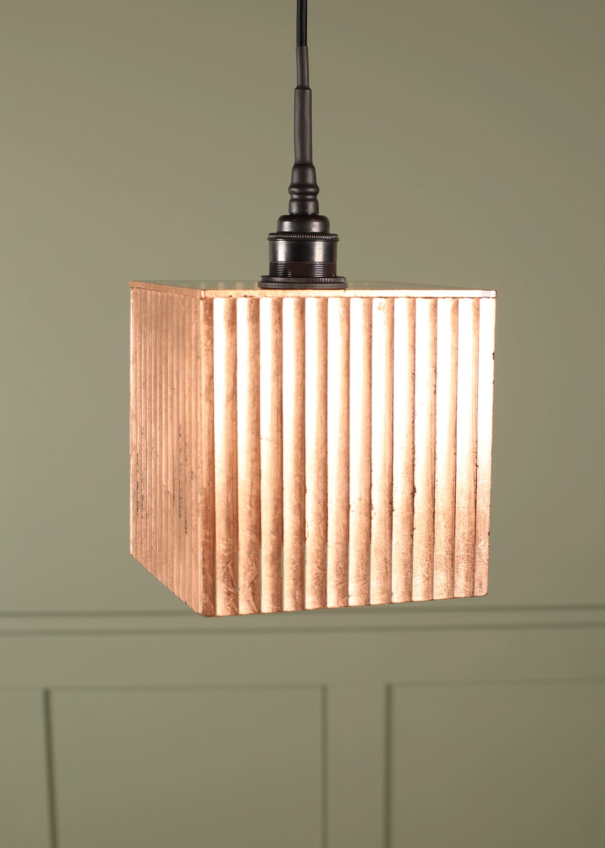Copper pendant light with a ribbed design on a green wall