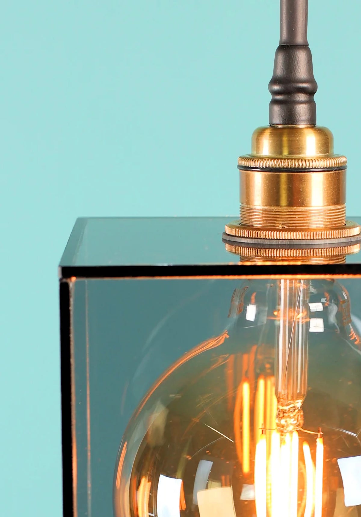 A close up of a smoked glass square pendant light brass lamp holder and Edison style light bulb