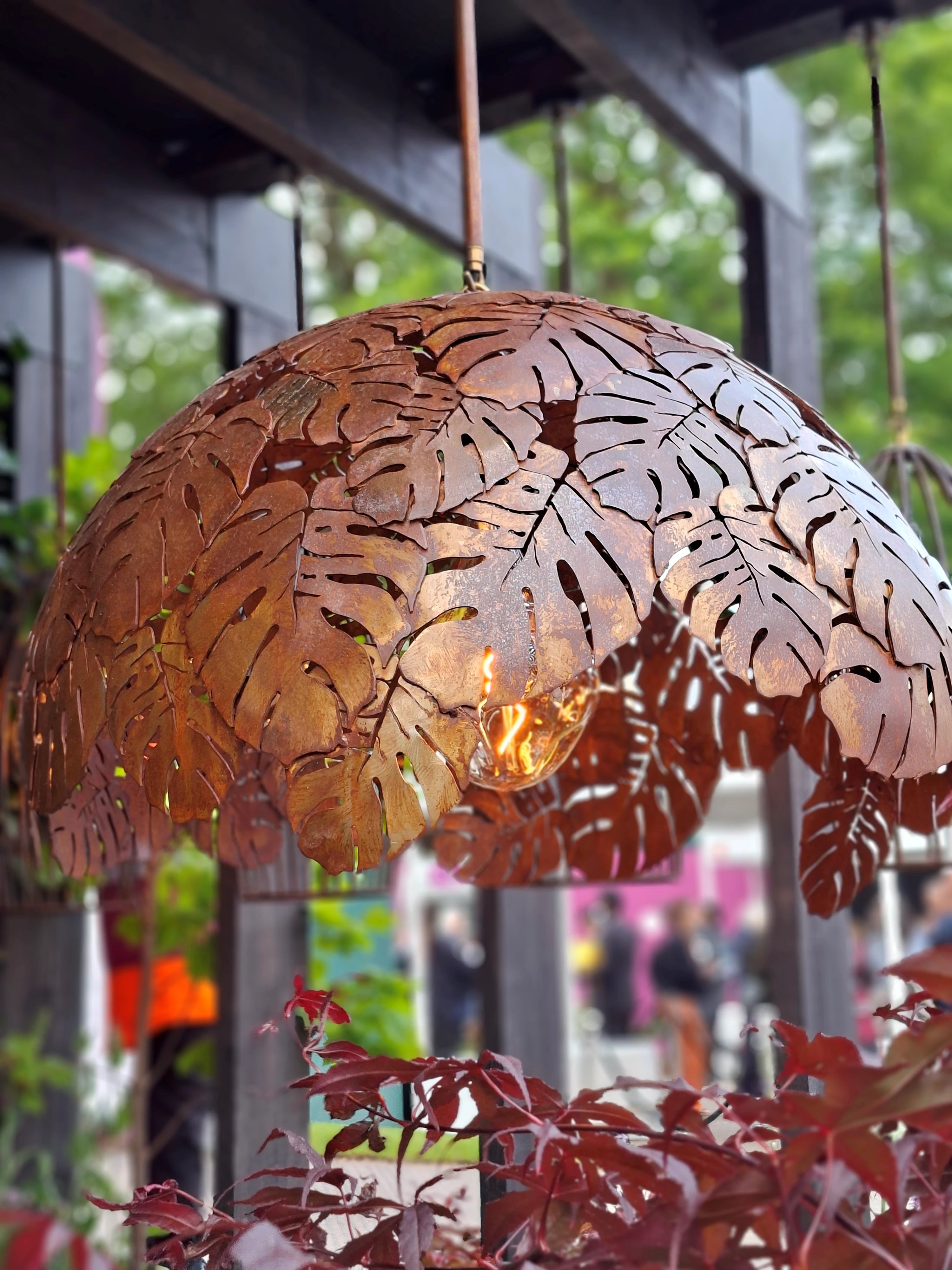 Decorative metal pendant light with leaf pattern hanging outdoors.