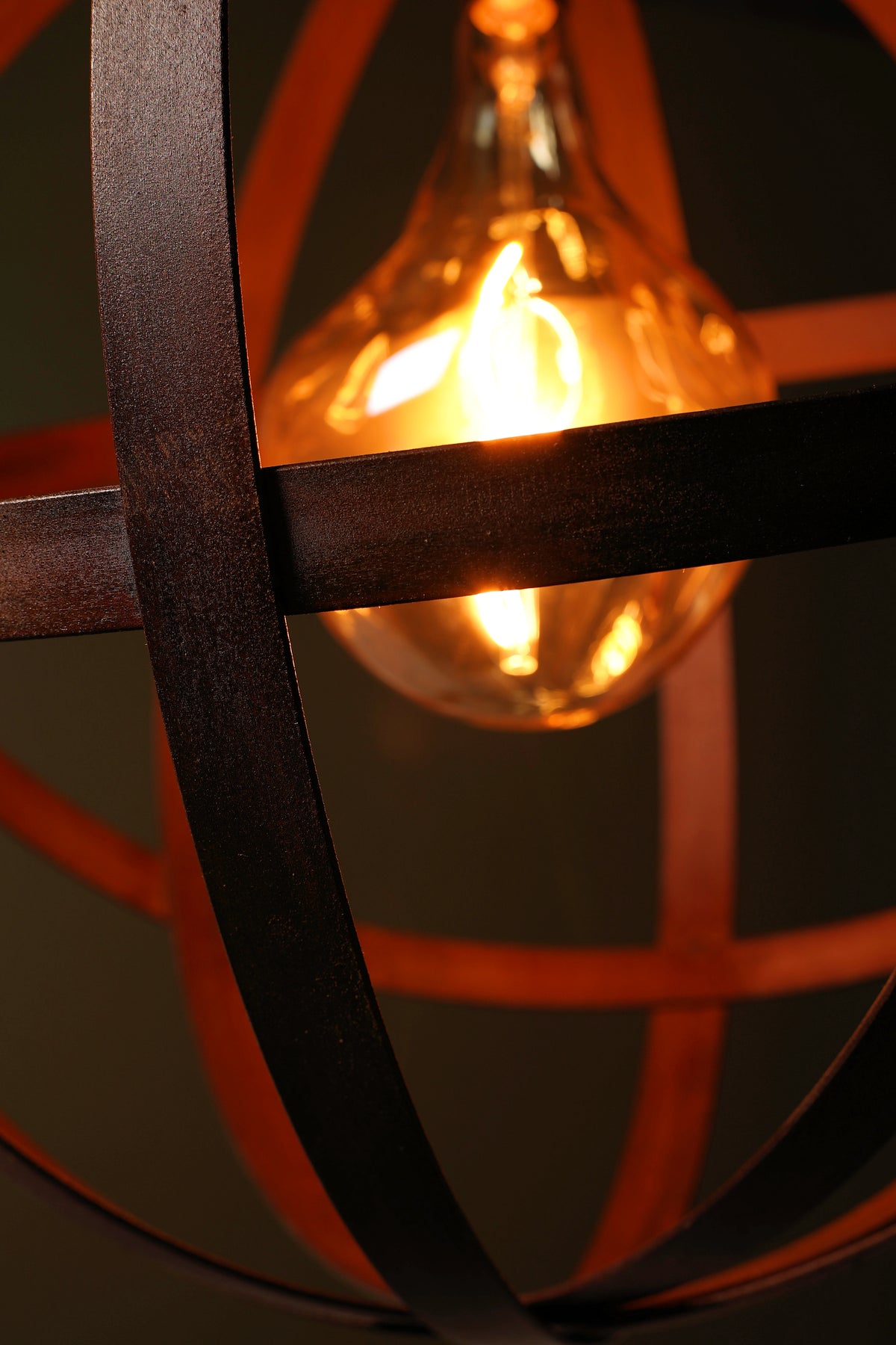 Close-up of a hanging light fixture with dark metal curved bars and a glowing warm amber bulb inside a glass globe shade.