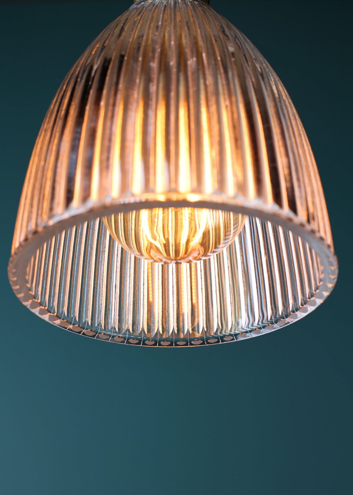 Close up of ribbed glass pendant on teal background
