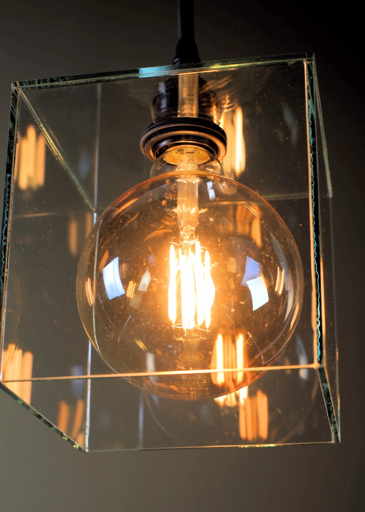 Vintage-style light bulb in a clear glass cube against a dark background