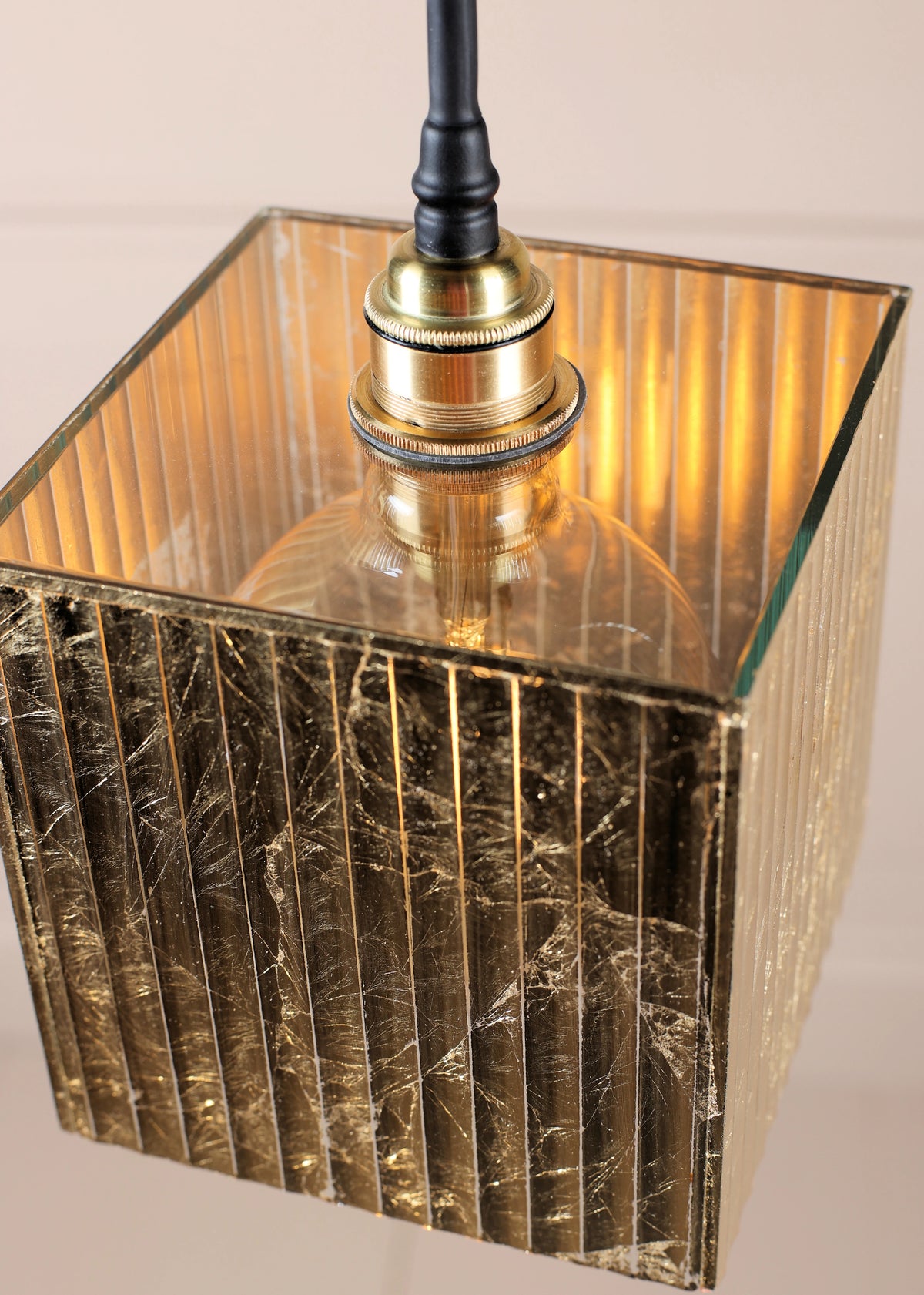 Close up of Edison style filament light bulb with gold ribbed glass light shade and brass fixings