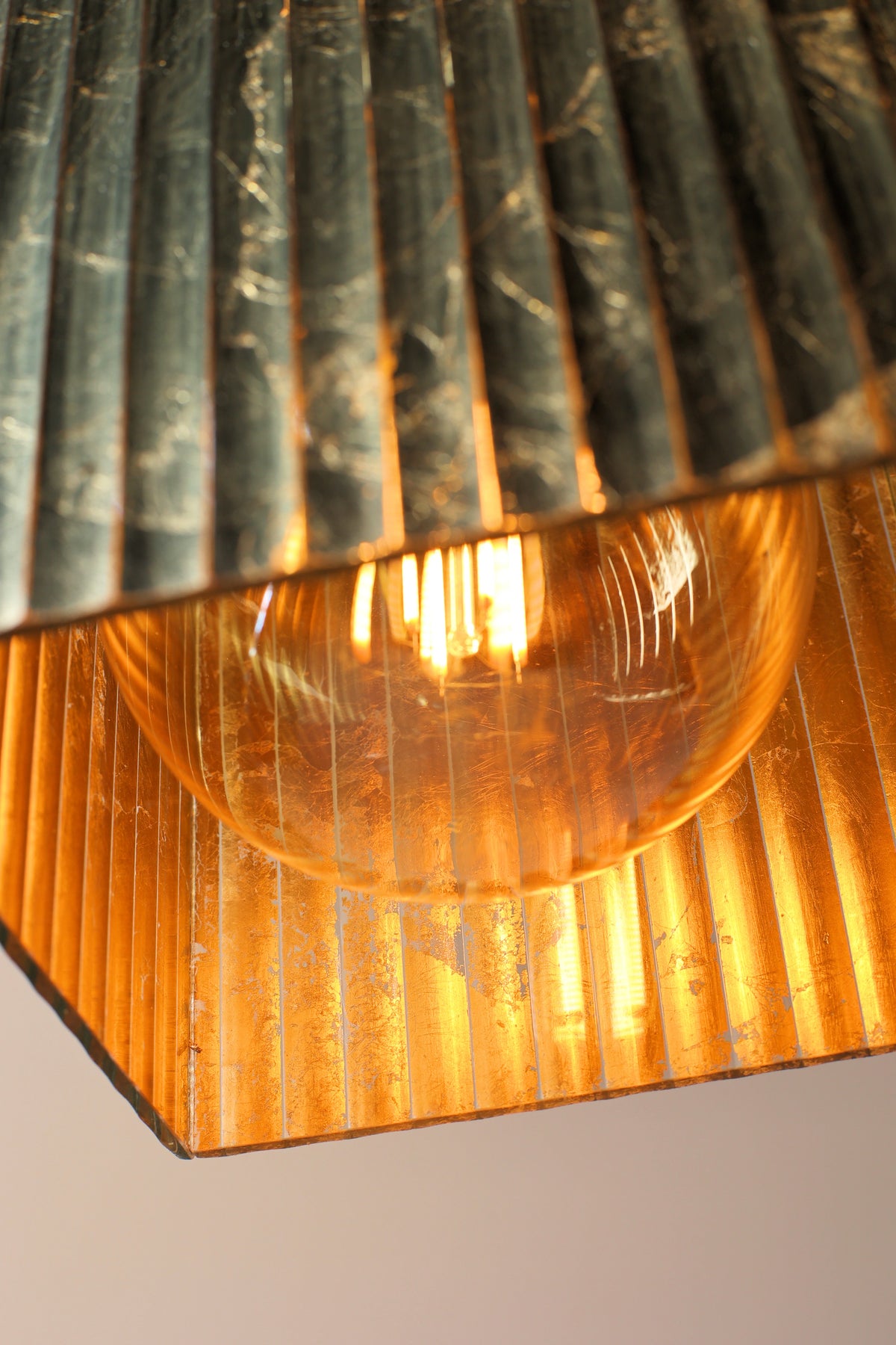 Close up of Edison style filament light bulb with gold ribbed glass light shade