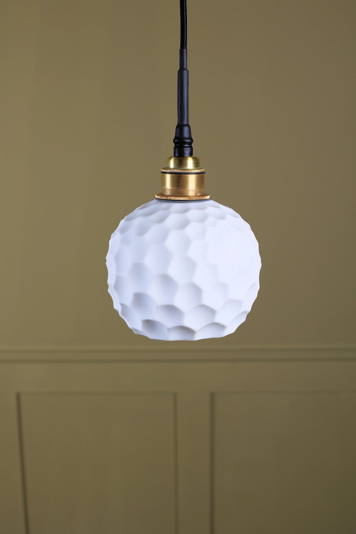 A ceramic beehive effect bathroom pendant light with brass lamp holder on dark olive background