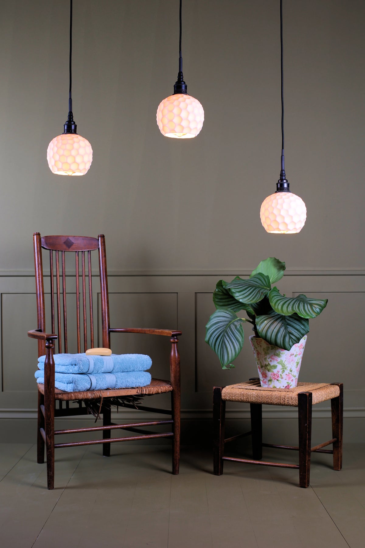 A cluster of ceramic beehive effect bathroom pendant lights hanging over wooden chair with pot plant and stool decoration