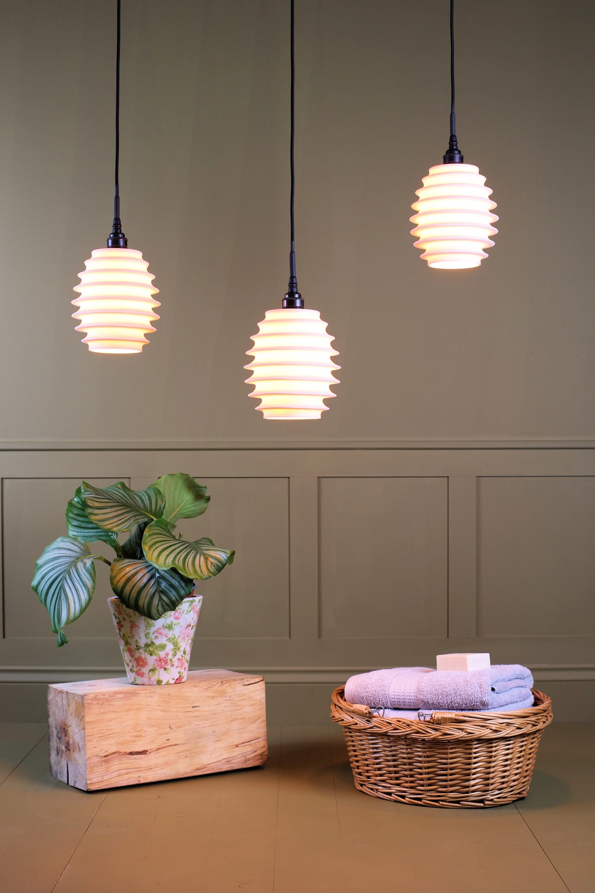 Concertina style porcelain triple cluster bathroom pendant lights with plant and basket of bath towels on sage green background